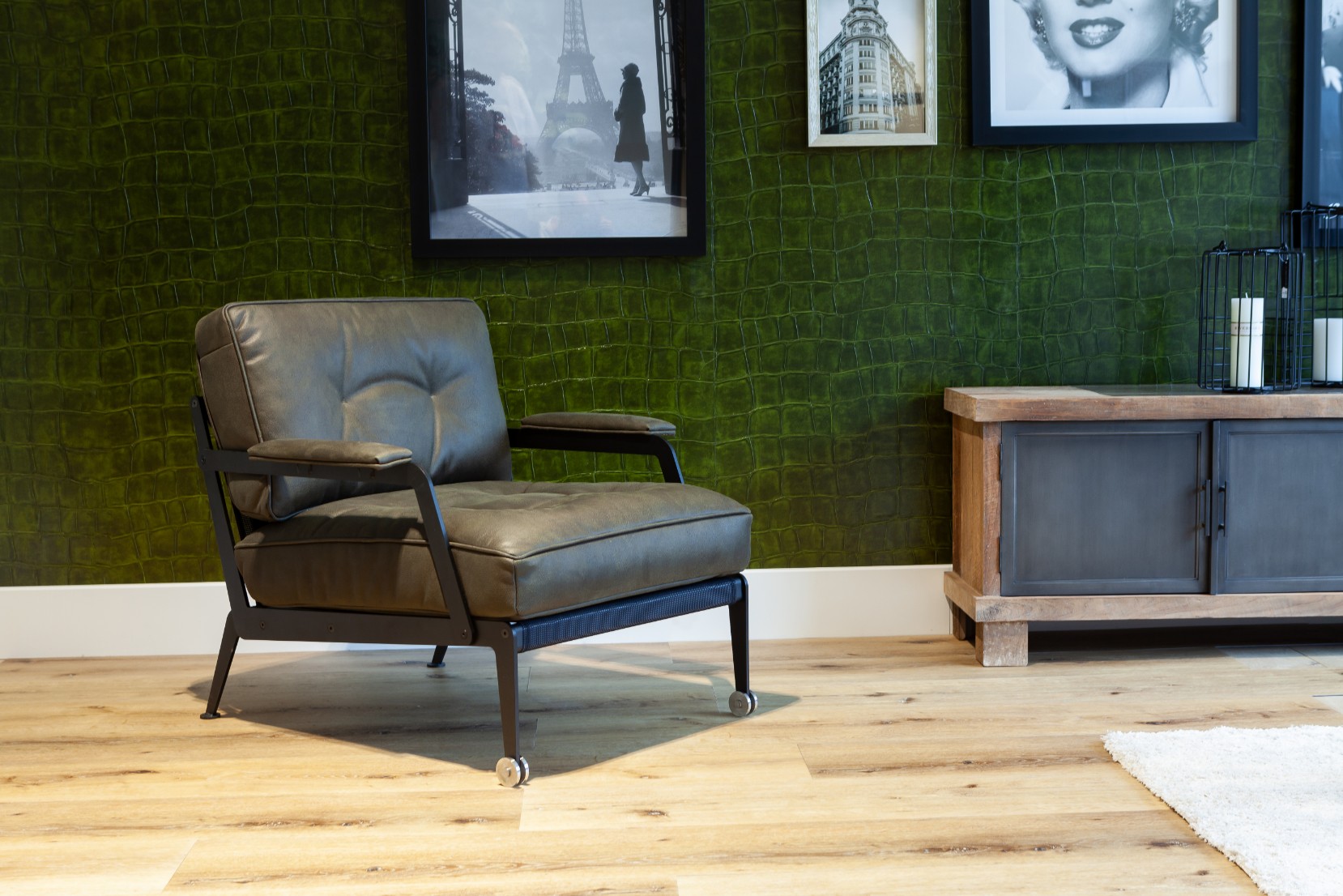 Grijze leren loungestoel op brede rustieke eiken planken voor een groene wand