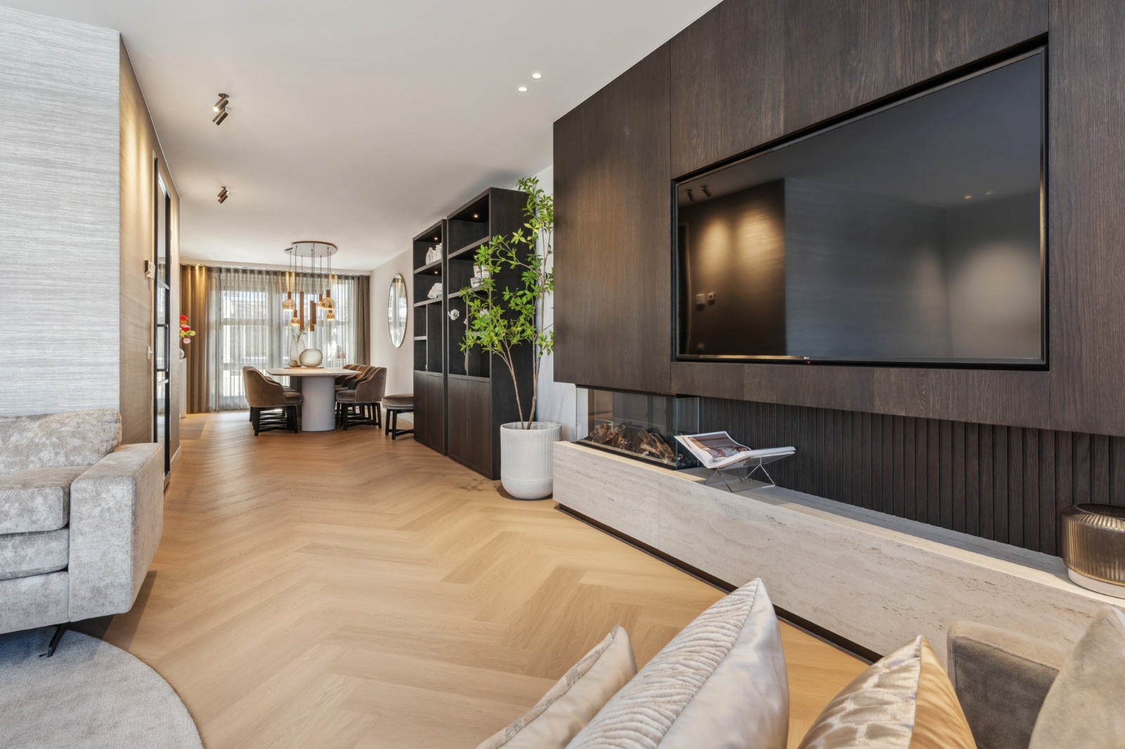 Sfeervolle woonkamer met licht eiken visgraatparket, een donkere houtwand met haard en een eethoek op de achtergrond