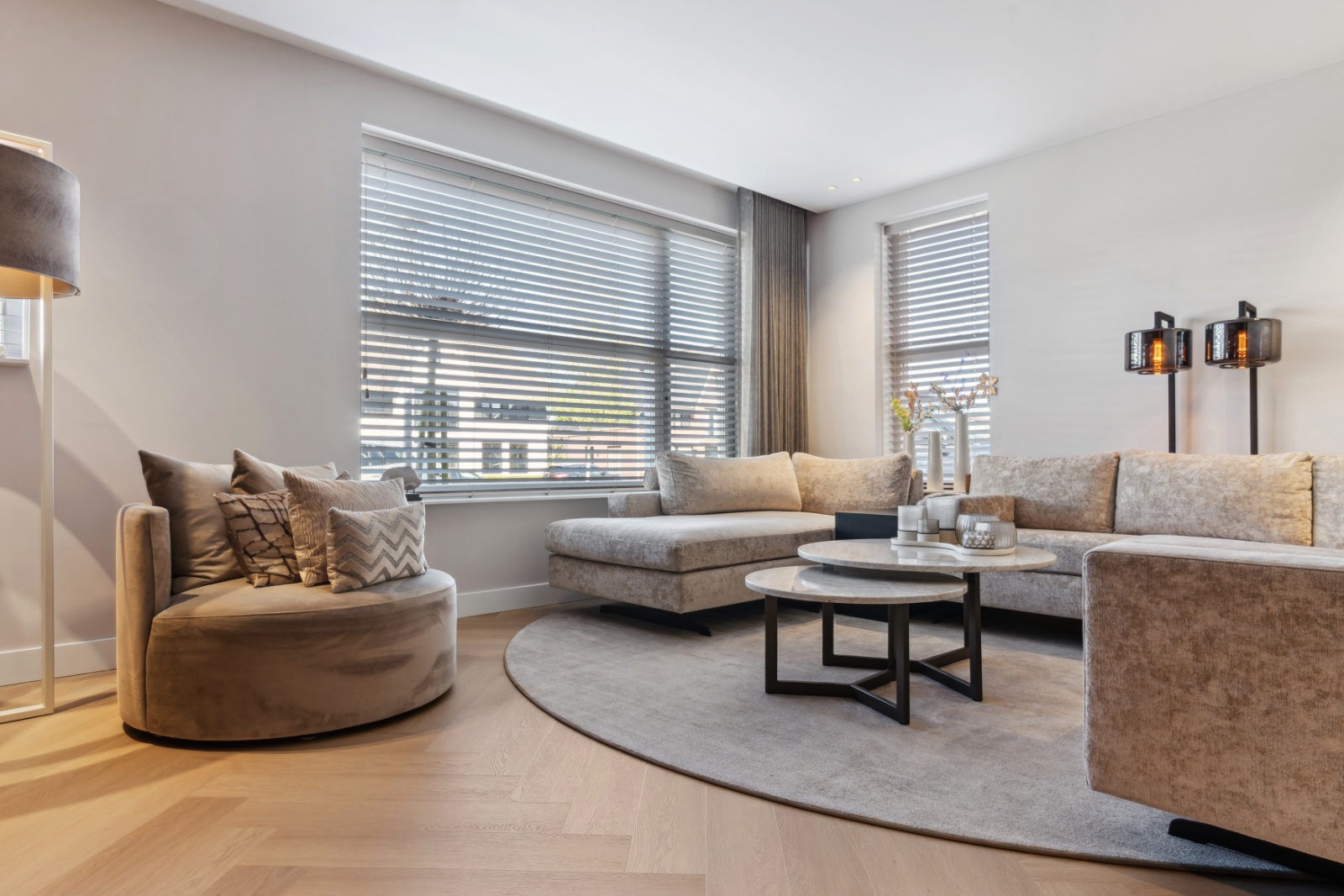 Lichte woonkamer met eiken visgraatvloer, taupe loungebank en marmeren salontafels
